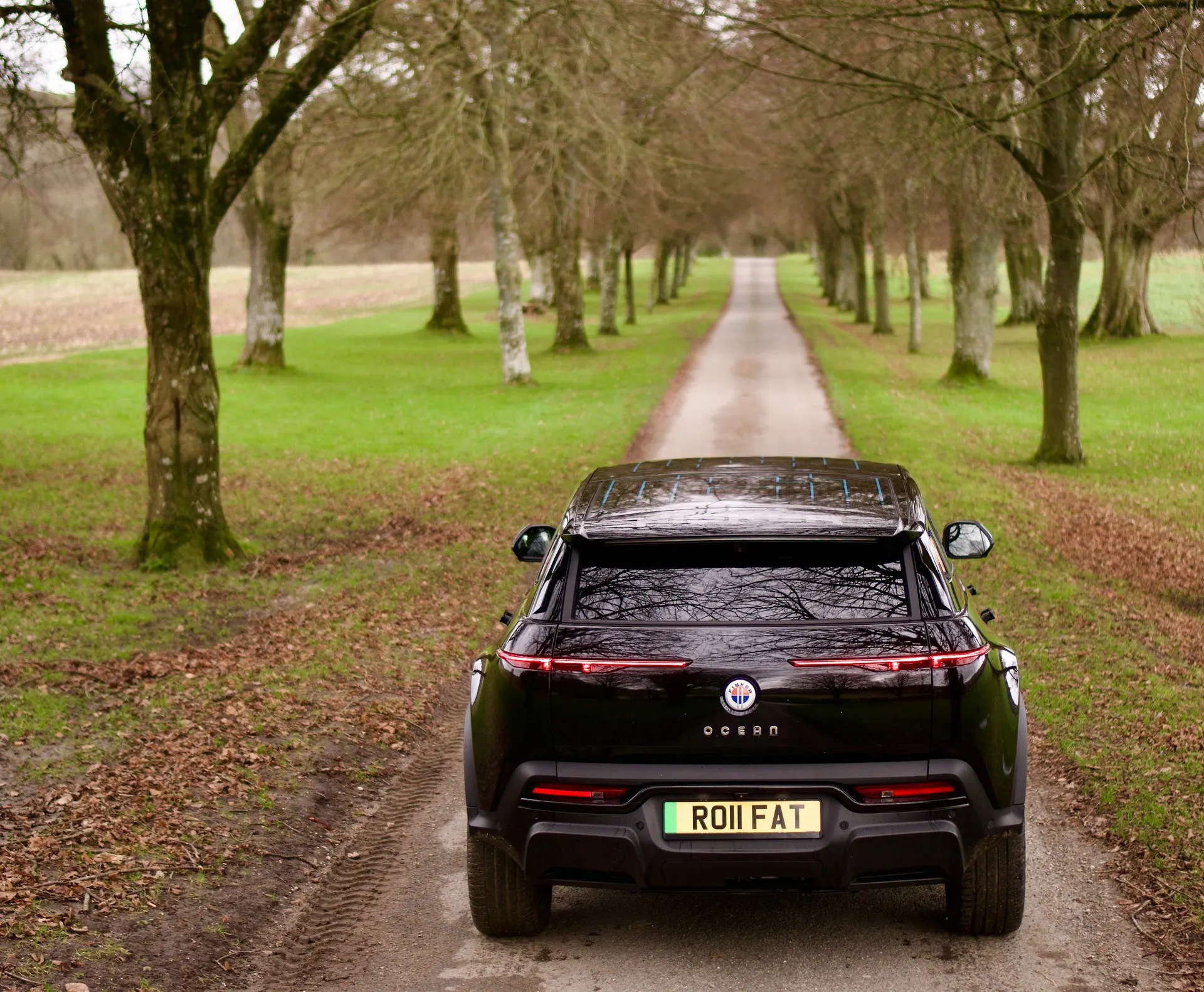 A black Fisker Ocean heading down a tree-lined lane